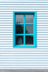 Side of a clapboard building with a window, painted blue.