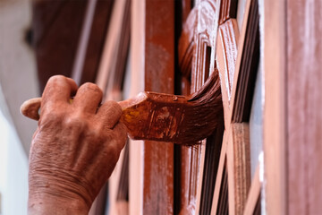 Hand holding a brush paint wooden window.