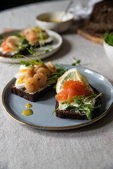 Smorrebrod dinner. Traditional Danish open rye bread sandwiches with smoked salmon and caviar and shrimps and egg, both with microgreens served on ceramic plates on linen tablecloth.