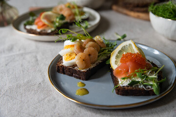 Smorrebrod dinner. Traditional Danish open rye bread sandwiches with smoked salmon and caviar and shrimps and egg, both with microgreens served on ceramic plates on linen tablecloth.