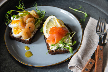 Smorrebrod dinner. Traditional Danish open rye bread sandwiches with smoked salmon and caviar and shrimps and egg served on ceramic plates on metal tray.