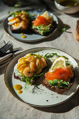 Smorrebrod dinner. Traditional Danish open rye bread sandwiches with smoked salmon and caviar and shrimps and egg, both with microgreens served on ceramic plates on linen tablecloth.