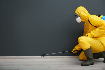 Obraz premium Pest control worker in protective suit spraying pesticide near black wall indoors. Space for text