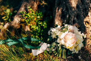 Obraz na płótnie Canvas bridal bouquet of white peonies and roses, branches of eucalyptus tree, with white and green ribbons on the grass near tree
