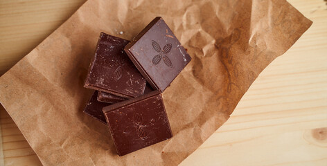 Pieces of chocolate bar lie on crafted brown paper. Close-up.With copy space.
