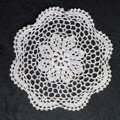 Vintage knitted napkin.
White handmade knitted coaster lace doily on a black background.