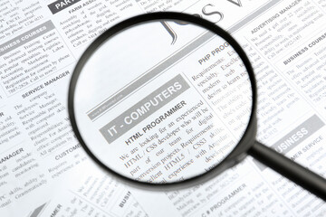 Looking through magnifying glass at newspaper, closeup. Job search concept