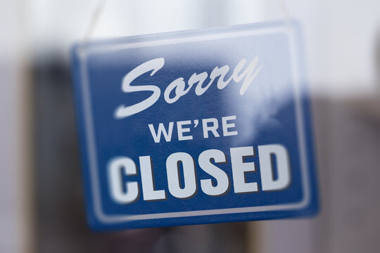 " Sorry we're closed " sign in blue and white, on shop glass door with white panels. Shallow depth of field.