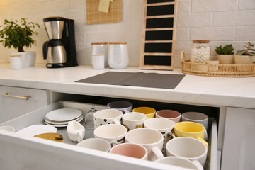 Fototapeta na wymiar Open drawer with cups and coffeemaker on countertop in kitchen