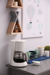 Modern coffeemaker and dishware on grey table in kitchen