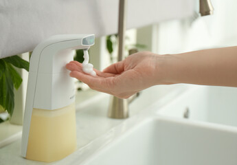 Woman using automatic soap dispenser in kitchen, closeup