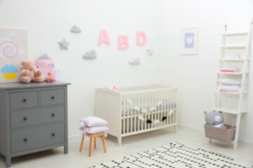 Blurred view of cute baby room interior with modern crib near white wall