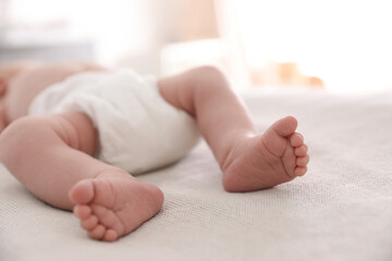 Cute little baby in diaper lying on bed in room, closeup