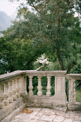Fototapeta na wymiar bridal bouquet of white and cream peonies, roses, veronica, delphinium, branches of eucalyptus tree with white ribbon on the railing of an ancient staircase