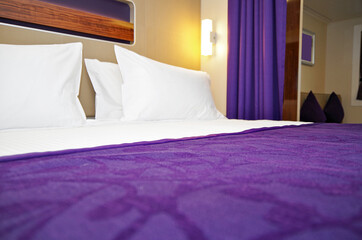 View of comfortable double bed inside ocean view or outside cabin or stateroom with purple day...
