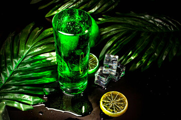 green drink in a glass, palm leaves, lemon and ice on a black background