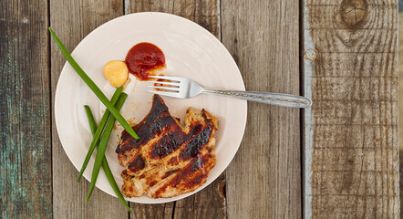 Ready pork steak in a white plate with green onions on an old wooden table. With copy space.