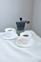 Two coffee cups and Italian coffee maker over table at home morning breakfast rituals concept, lifestyle food background.