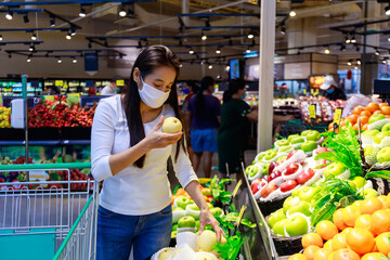 Asian woman wearing protective face mask push and hold shopping cart in supermarket department store. Girl, looking grocery to buy  some food. New normal after covid-19. Family concept.