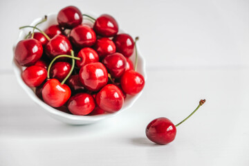 Obraz na płótnie Canvas Fresh juicy red cherries in a white plate on the white wooden background. Copy, empty space for text