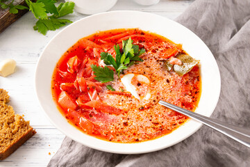 Russian traditional vegetable soup, borscht with sour cream and parsley in a white plate, spoon, on a gray napkin on a white background