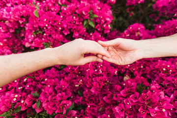 Fototapeta na wymiar Hands of a man and woman holding each other with a pink floral pattern as background