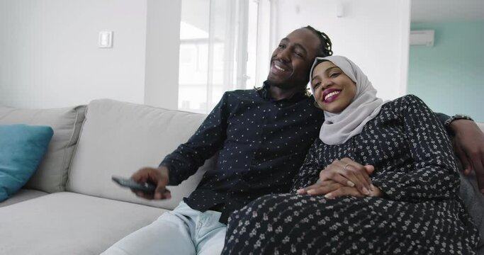 african couple on sofa in modern apartment watching tv