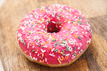 Pink doughnut with sprinkles on a wooden background