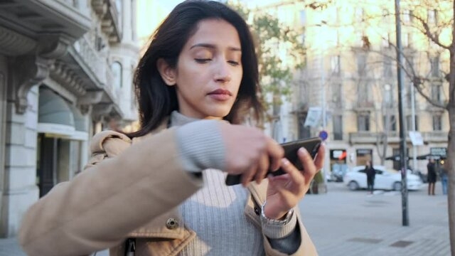 Video of pretty young woman using her mobile phone to consult the map while walking and looking around on the street.