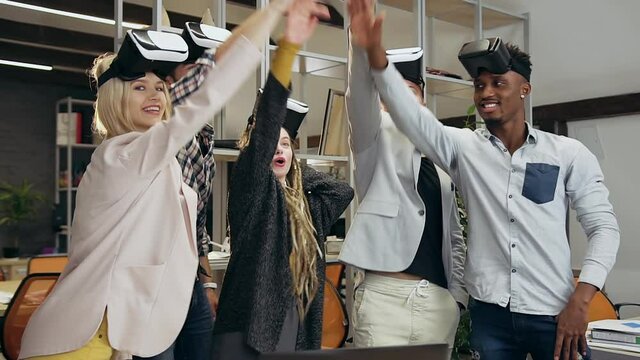Portrait of smiling likable young diverse modern team of workmates which putting hands on hands making unity business concept before start to work in special 3d glasses