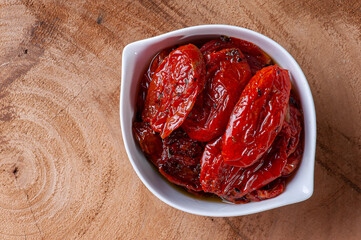 .Sun-dried tomatoes in a white bowl on a woody background. Top view