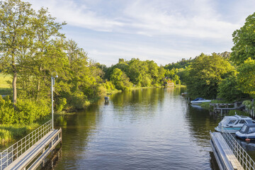 Beautiful landscape view of river with green forest trees on both sides and boats on blue sky background.