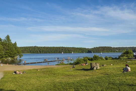 Gorgeous view of lake landscape. People on platform trying water. White sailboats on horizon. Sweden.