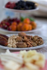 Preparation of Ramadan, Iftar Table. Dry date fruits, nuts, fig, almond, walnut, hazelnuts. The plate in the middle is in focus, rest are out of focus. Foreground, there are cheese, background fruits.