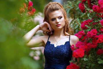 beautiful girl in a long evening dress in a beautiful garden with blooming roses