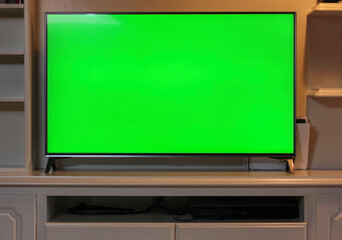 Close up of big green screen led TV in a cozy living room. Modern 55 inch sized television with chroma key green screen over a TV unit.