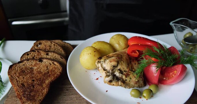 Cooking a delicious dinner. Baked chicken with vegetables. The dish is decorated with greens and olive. Spicy and refined taste. White dishes. Woman sprinkles the dish with spices. Bright colors.