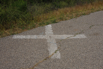 A large white cross sign on the pavement of an old country road with a brass nail in the middle as a geologic measurement and orientation marker visible from high in the air