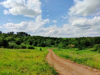 Fototapeta na wymiar winding road through a hilly green field against a blue cloudy sky