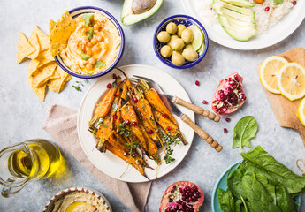 Variety of healthy vegan snacks, gourmet dips. Hummus,  roasted carrots, rice with tempeh in ceramic bowls viewed from above, plant based food
