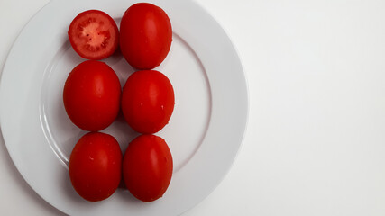 Six red ripe, juicy, wet, mouth-watering, healthy tomatoes on a white round porcelain plate. Place...