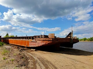 old abandoned barge on the sandy bank of the river against the blue sky on a sunny day