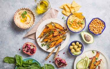 Variety of healthy vegan snacks, gourmet dips. Hummus,  roasted carrots, rice with tempeh in ceramic bowls viewed from above, plant based food