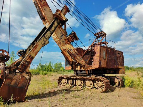 old mining excavator with peeling paint stands in a field against a blue sky with clouds on a sunny day