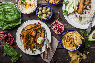 Variety of healthy vegan snacks, gourmet dips. Hummus,  roasted carrots, rice with tempeh in ceramic bowls viewed from above, plant based food