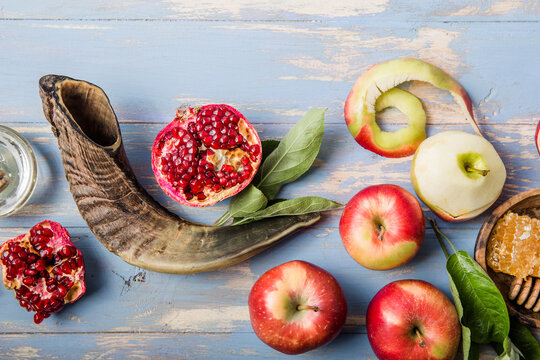 Rosh hashanah  (Hashana) - jewish New Year holiday concept. Traditional symbols: Honey jar and fresh apples with pomegranate and shofar - horn on a blue background.  View from above