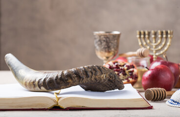 Rosh hashanah - jewish New Year holiday concept. Traditional symbols: Honey jar and fresh apples with pomegranate and shofar-horn, Prayer book  on a concrte   background. Copy space for text. 