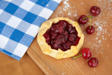Summer homemade baked galette tart open pie curd biscuit Breton crepe, Savory Buckwheat Galettes Bretonnes with cherries on wooden background. 
Blue and white checkered napkin Summer pie.