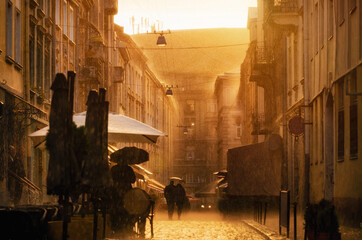 Couple with umbrella walking down evening street under heavy rain. Sunlight highlights raindrops of rain. Lviv, Ukraine.