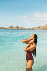 Woman in red swimsuit enjoying in transparent turquoise ocean water with mountain view. Travel and vacations concept. Beauty and wellness. Tropical background with empty space.
